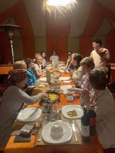 a group of people sitting at a long table eating food at Sahara Happy Camp in Merzouga