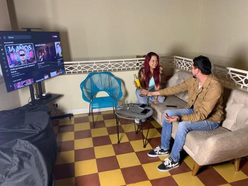 a man and woman sitting in a living room with a tv at Lucca Hostel Medellín in Medellín