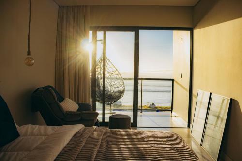 a bedroom with a bed and a chair and a window at Austral Suítes à Beira-Mar in Imbituba