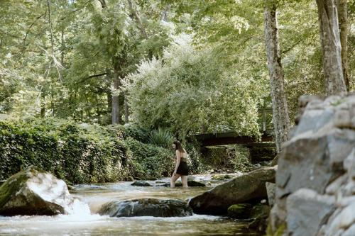 a woman walking across a stream in a forest at Creekside Modern Tiny Home - Firepit - Racoon Cabin in Gatlinburg