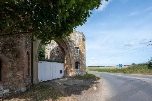 an old stone building with a white gate on the side of a road at Ivy Lodge in Rendlesham
