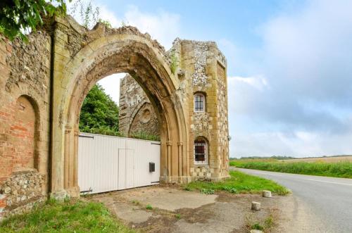 an old stone building with a white gate and a road at Ivy Lodge in Rendlesham