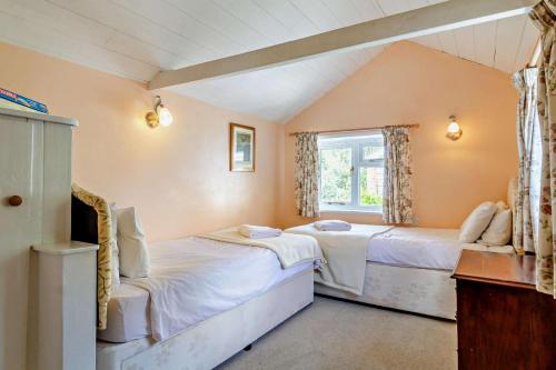 two beds in a room with a window at Coach House Cottage in Wickham Market