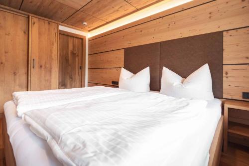 a bedroom with a large white bed with wooden walls at Appartement Pension Strolz in Bichlbach
