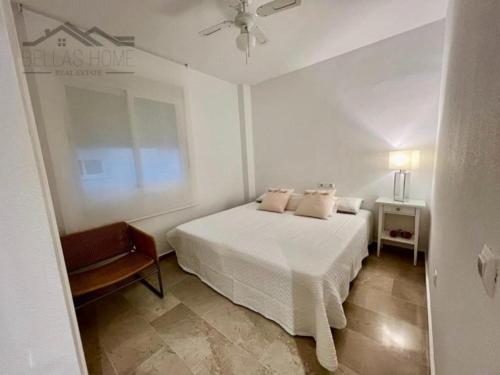 a white bedroom with a bed and a chair at Faro Bay in Estepona