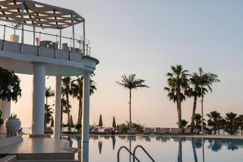 a swimming pool with palm trees and a building at The Noverian Scenic Crete 5 Star Hilltop Villa Resort & Spa in Malia