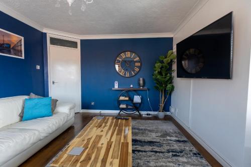 a living room with a white couch and a clock at Hullidays - 'Old School Penthouse' Trinity Square in Hull