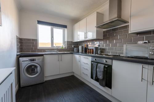 a kitchen with white cabinets and a washer and dryer at Hullidays - 'Old School Penthouse' Trinity Square in Hull