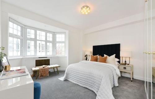 a white bedroom with a large bed and windows at Estatesmen Harrods Knightsbridge Apartment in London