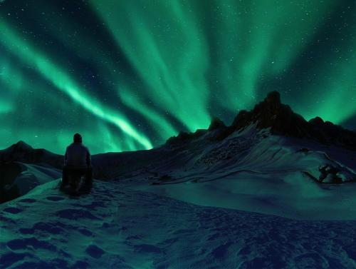 a man standing in the snow watching the northern lights at LUXURIOUS COMFORTABLE Family Villaes in Akureyri