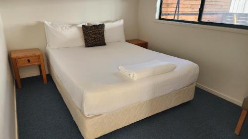 a bedroom with a bed with white sheets and a window at T's Resort & Motel in Port Macquarie