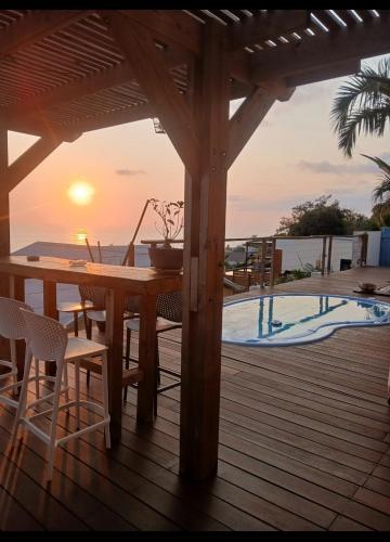 a wooden deck with a table and chairs and the sunset at Terasse altitude in Saint-Leu