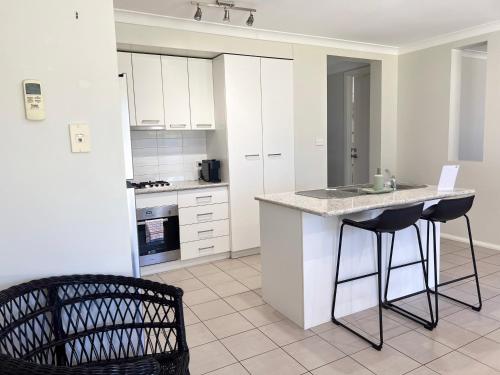 a kitchen with white cabinets and a counter with two bar stools at Boorooma Bliss in North Wagga