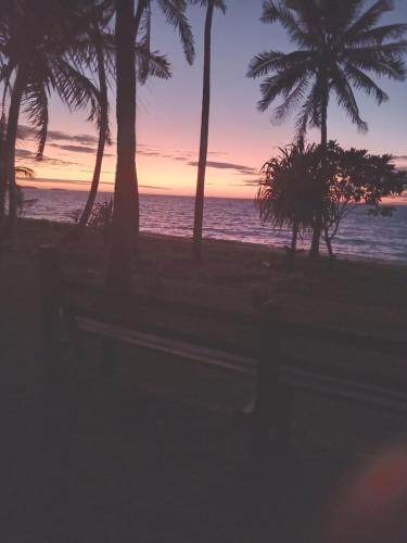 a bench on a beach with palm trees and the ocean at Nenas Homestay 