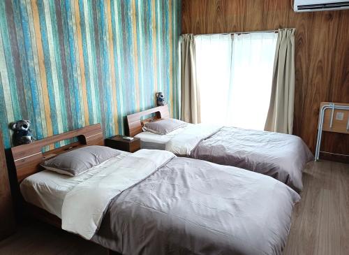 two beds in a hotel room with a window at させぼ旅の宿KawashimoEn in Sasebo