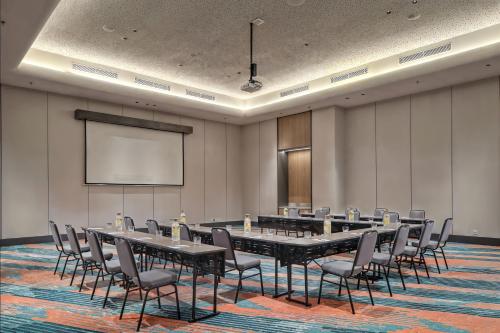 a conference room with tables and chairs and a screen at Aloft Surabaya Pakuwon City in Surabaya