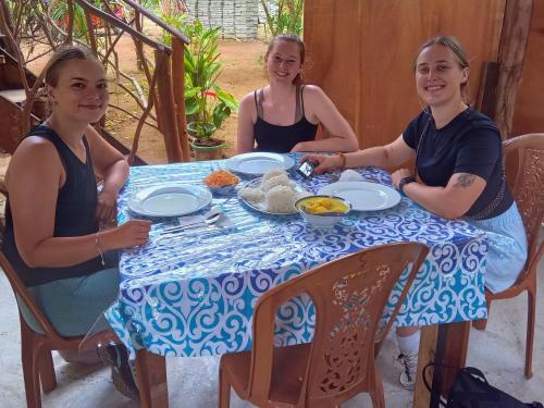 Drei Frauen sitzen an einem Tisch mit Essen drauf. in der Unterkunft The Travel Tree Hostel in Sigiriya
