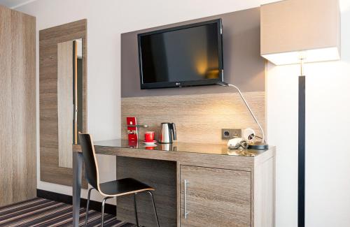 a room with a desk with a tv and a chair at Leonardo Hotel Nürnberg in Nürnberg