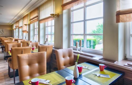 a dining room with tables and chairs and windows at Leonardo Hotel Hamburg Stillhorn in Hamburg