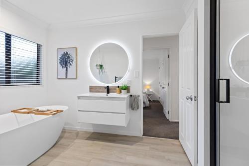 a white bathroom with a sink and a mirror at JB's Sanctuary - Papamoa Holiday Home in Papamoa