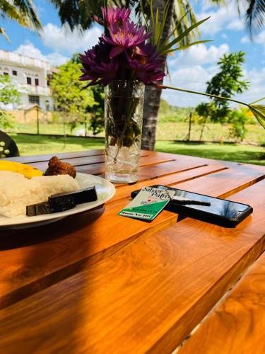 a table with a plate of food and a vase with flowers at Silver Palm Resort Anuradhapura in Anuradhapura