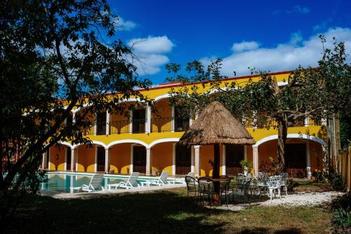 a yellow building with a pool and tables and chairs at Hotel Tuul in Izamal
