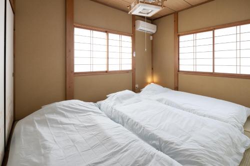 two white beds in a room with two windows at A home ゲストハウスすえ in Mashizume