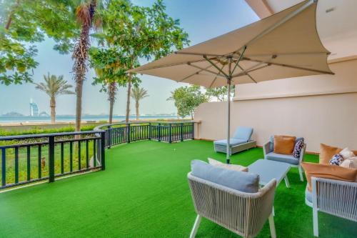 a patio with chairs and an umbrella and grass at Luxe Getaways Royal Amwaj Palm Jumeirah Resort Apartment Holiday Home in Dubai