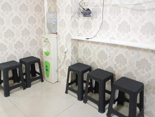 a kitchen with three black stools next to a refrigerator at RedDoorz Hostel at Luna Bunkbed Malioboro in Jarakan