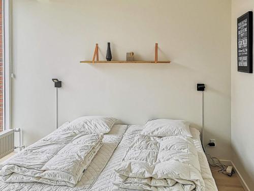 an unmade bed in a white bedroom with a shelf at Luxury Spa Apartment in Sondervig - By Traum Ferienwohnungen in Ringkøbing