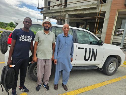 three men are standing in front of a car at StayNova - Transit Apartment near Motorways & Airport in Islamabad