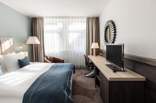 a hotel room with a bed and a desk with a television at Garner Hotel Essen - Handelshof by IHG in Essen