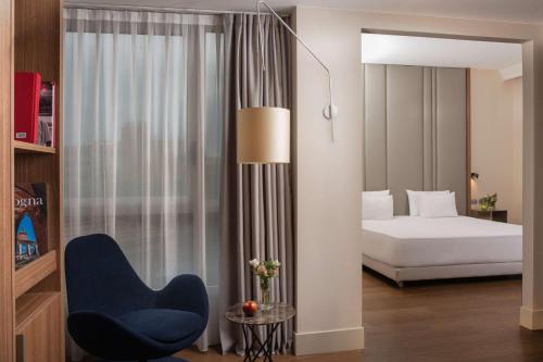 a bedroom with a bed and a blue chair at NH Bologna De La Gare in Bologna