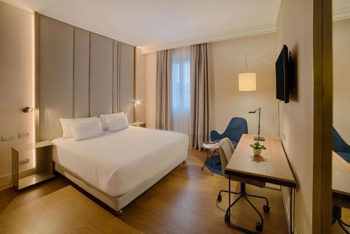 a hotel room with a white bed and a desk at NH Bologna De La Gare in Bologna