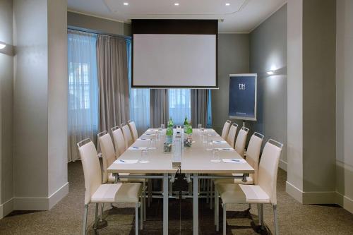 a conference room with a long table and a projector screen at NH Bologna De La Gare in Bologna