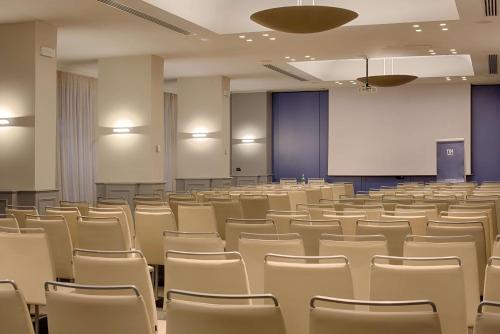 an empty lecture room with white chairs and a podium at NH Bologna De La Gare in Bologna