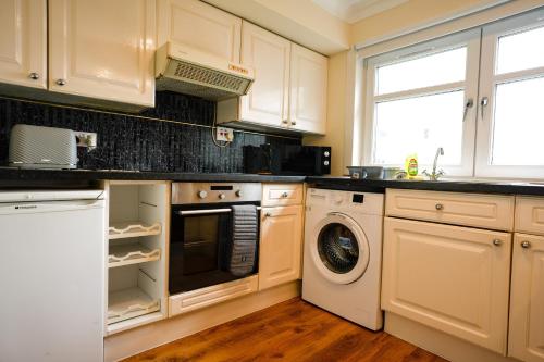een keuken met witte kasten en een wasmachine en droger bij 2 BDR Apt At Caledonia Luxe Stays Short Lets & Serviced Accommodation Airdrie in Airdrie