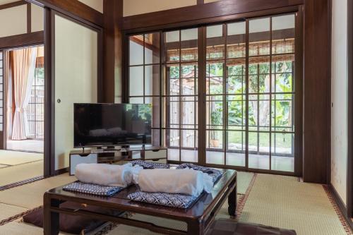 a living room with a tv and large windows at Furusato Matcha Cafe & Ryokan Chiangmai in Ban Pang Champi