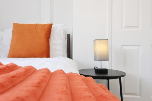 a bed with an orange pillow and a table with a lamp at King Beds - Dining Space - Ev Charger - Coffee - Contractor & Families in Coity