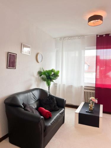 a living room with a black leather couch and a table at Helle 2 Zimmer Wohnung mit Balkon gemütlich & zentral in Aalen
