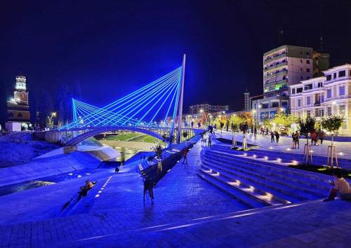 a bridge over a river with people sitting on benches at night at Ermal's House in Fier