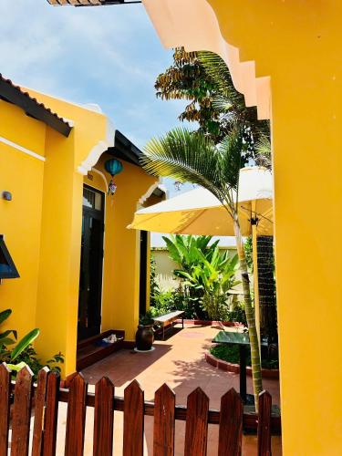 a yellow house with a palm tree and umbrella at Laa House in Hoi An