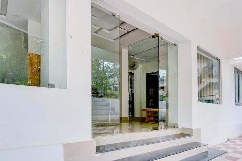 a glass pivot door in a white house with a staircase at Super Hotel O Kazhakootam Near Technopark Phase 2 in Trivandrum