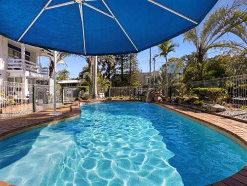 a blue swimming pool with a blue umbrella at The Bay Beach Shack, Hervey Bay in Hervey Bay