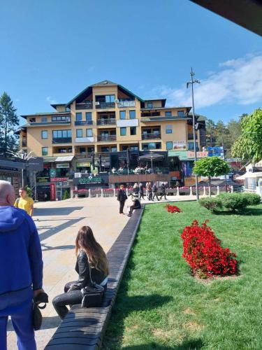 a woman sitting on a bench in front of a building at Apartman Centar Vila Jezero in Zlatibor