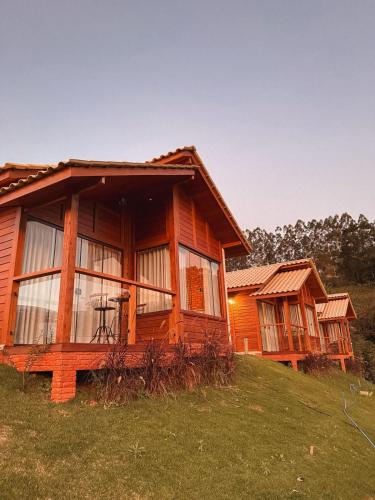 a log cabin on a grassy hill with two houses at Domus Fiorese Chalés in Venda Nova do Imigrante