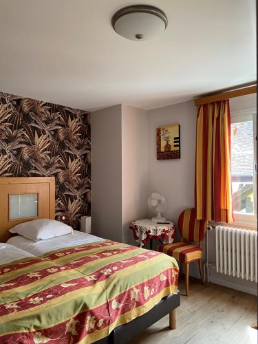a bedroom with a bed and a chair and a window at Hotel Au Cerf in Riquewihr