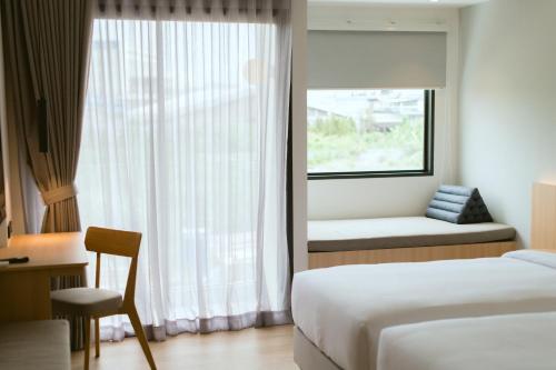 a bedroom with a bed and a window with a chair at PAAK Hotel Suvarnabhumi in Lat Krabang