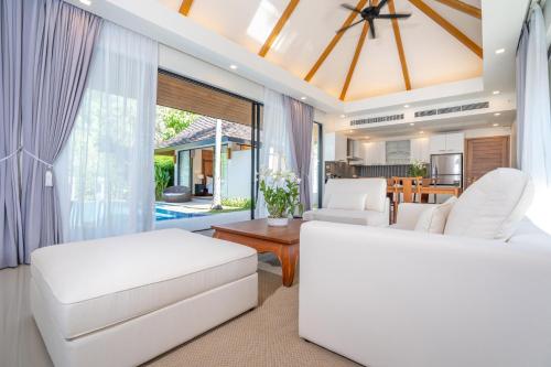 un salon avec des meubles blancs et une grande fenêtre dans l'établissement Anchan Villas Phuket - Private 2 Bedroom Pool Villas by Escape Villas, à Ban Phru Champa