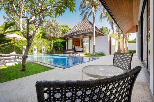a patio with a table and chairs next to a swimming pool at Anchan Villas Phuket - Private 2 Bedroom Pool Villas by Escape Villas in Bang Tao Beach